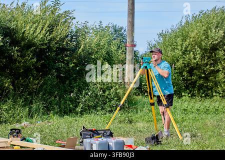 Surveyor operates precision instrument mounted on yellow tripod outdoors, focusing on distant target point. Stock Photo