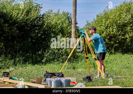 Field specialist uses optical surveying device to measure elevation differences across landscape area. Stock Photo