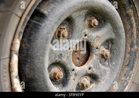A detailed close-up shot of an old, damaged stamped steel wheel rim covered in deep rust, flaking paint, and corrosion. The five wheel nuts and studs Stock Photo