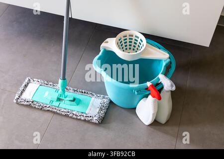 A modern mop with a microfiber head rests beside a turquoise bucket and two spray bottles, ready for household chores Stock Photo
