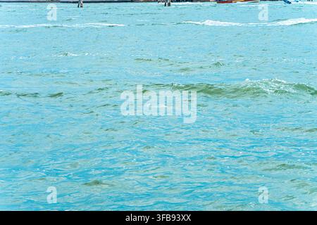 Turquoise ocean water ripples gently beneath distant boats near the horizon. Stock Photo
