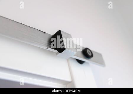 Close-up view of a contemporary sliding door mechanism featuring a brushed metal rail and black roller assembly Stock Photo