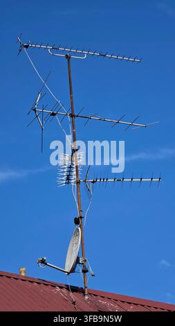 Rooftop array of television antennas and a small satellite dish mounted on a post against a clear blue sky Stock Photo