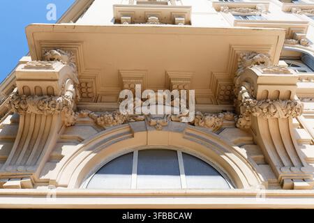 Close-up of an ornate Belle Epoque cornice and balcony support in Antibes, France, with carved garlands and a curved stone facade under blue sky. Stock Photo