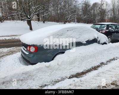 A blue sedan car heavily covered in thick snow parked on the side of a residential street during winter. The vehicle is almost completely buried with Stock Photo