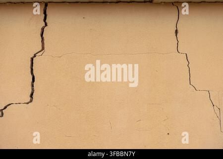 A close-up view of a textured beige wall with prominent cracks, indicating structural issues and the passage of time Stock Photo