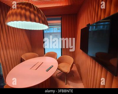 A modern meeting room with a monochromatic orange and coral color scheme featuring an oval pink table surrounded by three orange upholstered chairs Stock Photo