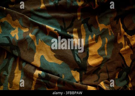 Full-frame texture of rumpled camouflage fabric featuring classic military green, brown, and tan tones. Top view. Stock Photo