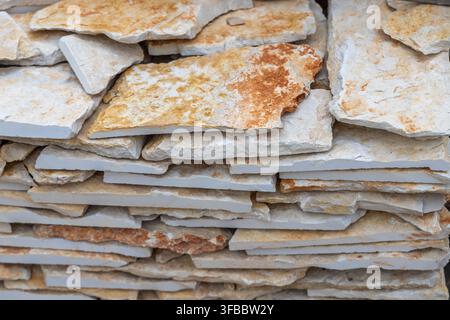 A close-up view showcases a neatly stacked pile of irregular, flat stone pieces exhibiting varied textures and warm, natural coloration Stock Photo