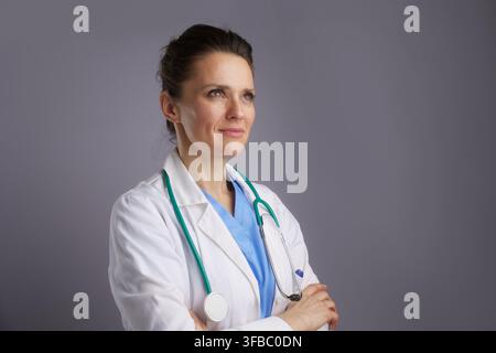 An adult female doctor in a lab coat and stethoscope gazes upward and right with a thoughtful and optimistic expression, symbolizing the future of med Stock Photo