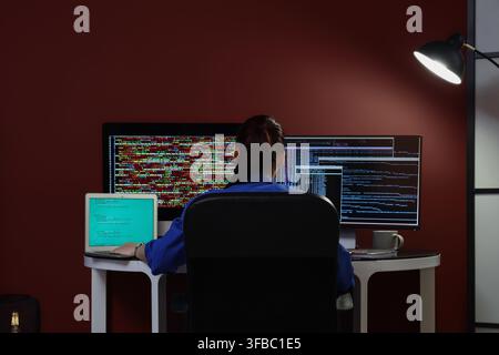 Software development and coding, woman programmer working late on multiple screens with complex code in a dark office Stock Photo