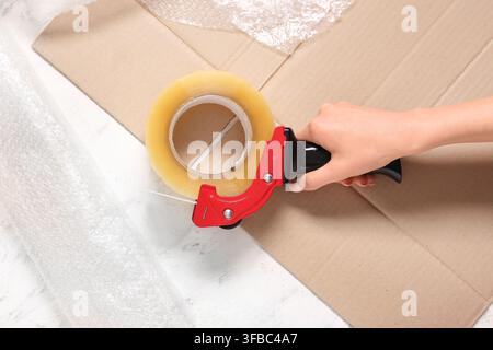 Shipping and packaging supplies, hand using a tape dispenser on cardboard box with bubble wrap for secure delivery Stock Photo