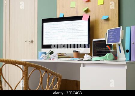 Software development and coding workspace, modern home office with multiple screens displaying code and sticky notes on a wooden board Stock Photo