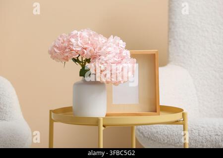 Vase with pink hydrangea flowers and frame on table in living room Stock Photo