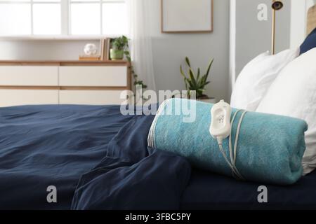 Folded electric heating pad on bed in room Stock Photo