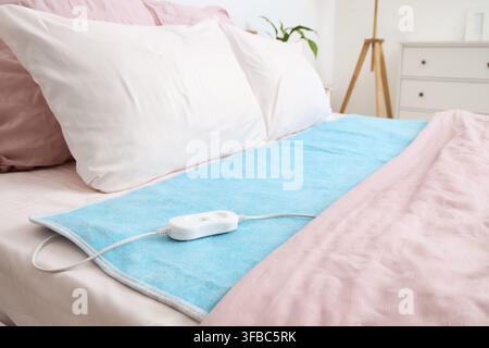 Modern electric heating pad on bed in room Stock Photo
