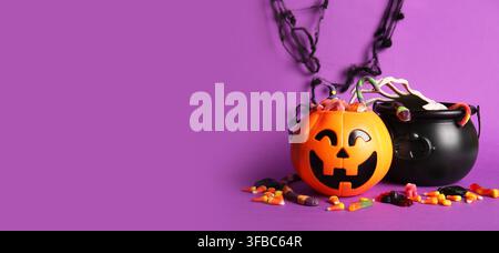 Halloween celebration and trick or treat concept, pumpkin bucket and cauldron filled with candy on a purple background with copy space Stock Photo