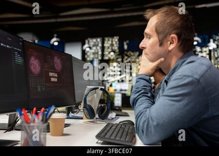 Programmer at office desk thinking how to fix critical error warning displayed on computer. Tech company IT employee brainstorming how to fix computer bug affecting server network Stock Photo