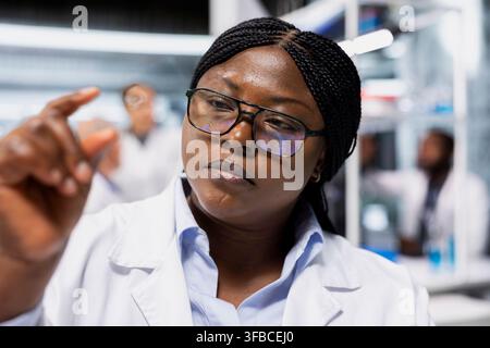 Close up of nanotechnology scientist examining DNA sample on microscope slide for mutation analysis. Lab employee checking biological specimen preparation before high tech imaging process Stock Photo