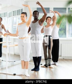Group mastering third position at barre in ballet studio Stock Photo