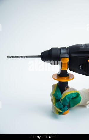 A gloved hand holds the black rotary hammer assist handle with orange accents and a drill bit firmly Stock Photo
