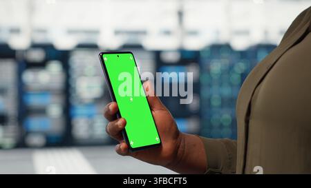 Close up of admin working in data center using isolated screen smartphone to optimize network infrastructure. Server farm worker diagnosing hardware malfunctions using mockup mobile phone Stock Photo