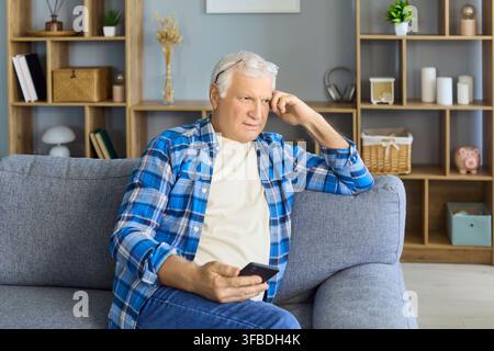 Senior man using smartphone on sofa at home, relaxing and reading messages online Stock Photo