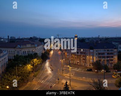 City street at dusk with light trails and tall buildings Stock Photo