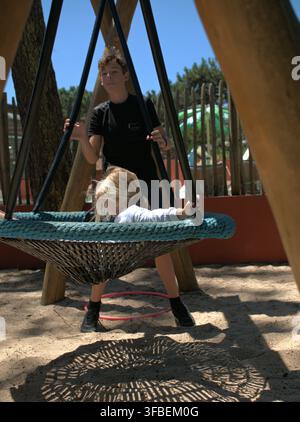 Boy pushing empty side of nest swing with hoop on the sand Stock Photo