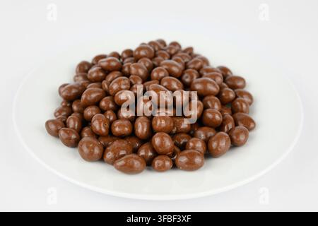 Milk Chocolate Covered Peanuts on a plate on a white background Stock Photo