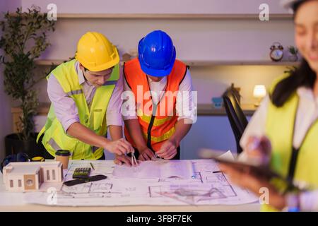 Asian engineers measuring architectural blueprints with compass on office desk Stock Photo