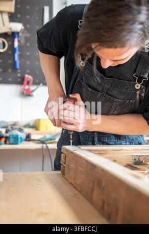 Focused master using electric cordless drill instrument and fastens metal screw in corner of frame. Stock Photo