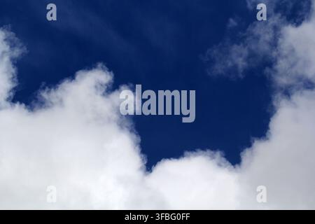 A vibrant, deep blue sky framed by fluffy white cumulus clouds on a bright, sunny day Stock Photo