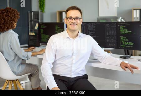 Smiling male programmer in office with code on monitors confident software engineer Stock Photo