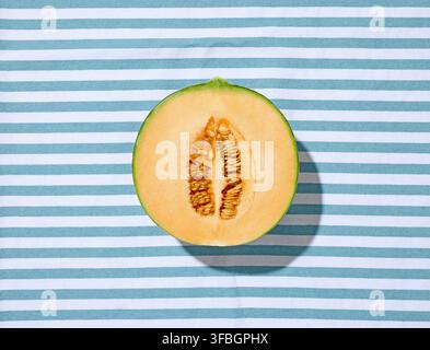 Fresh ripe melon half placed on a striped tablecloth and illuminated by warm natural sunlight, photographed from above, creating a bright and summery Stock Photo