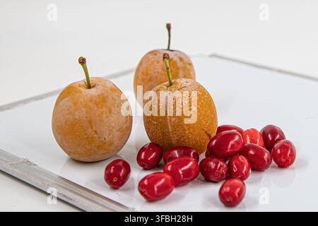 Three Fresh Yellow Plums with Ripe Cornelian Cherries on White Surface Stock Photo