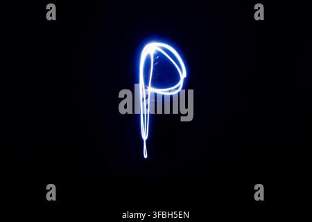 Long exposure photography capturing glowing white and blue light painting forming the letter P isolated on dark black background. Stock Photo