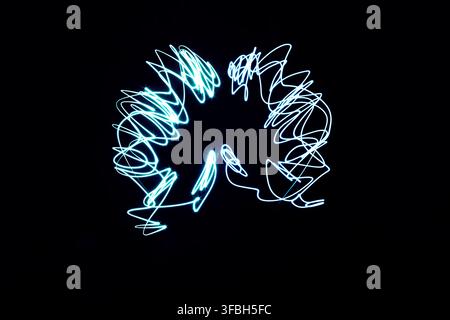 Abstract long exposure light painting forming the delicate shape of glowing blue wings against a deep black background in a studio darkroom setup. Stock Photo