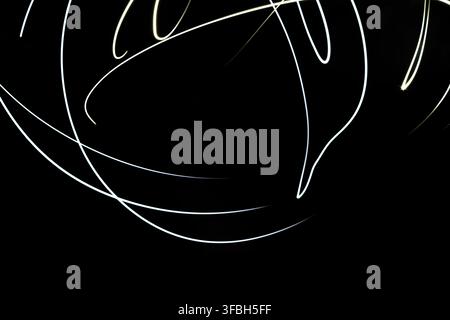 Abstract photography featuring glowing white curved light trails forming dynamic graceful patterns against a dark solid background in a studio setting Stock Photo