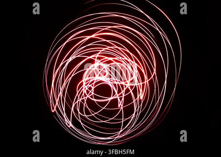 Abstract long exposure photography capturing vibrant red light trails creating circular patterns and dynamic swirling streaks against a solid black ba Stock Photo