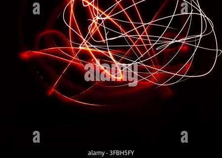 Abstract long exposure photography capturing glowing red and white light trails moving dynamically across a deep black background, creating vibrant lu Stock Photo