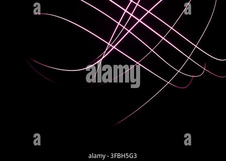 Abstract long exposure light painting with glowing pink curved lines forming geometric patterns on a dark background. Stock Photo