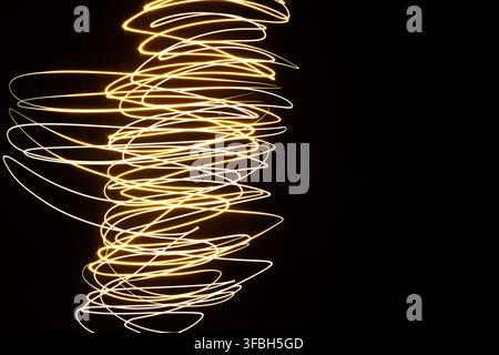 Abstract long exposure photography capturing intricate golden light trails forming a swirling spiral pattern against a solid dark black background. Stock Photo