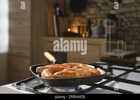 Homemade sausages in cast-iron skillet on gas stove. Grilling banger sausages in griddle pan at home Stock Photo