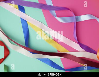 Many silk multi-colored ribbons on a colored background, top view Stock Photo