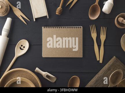 Open empty paper notebook and wooden kitchen items on a black wooden table, top view Stock Photo
