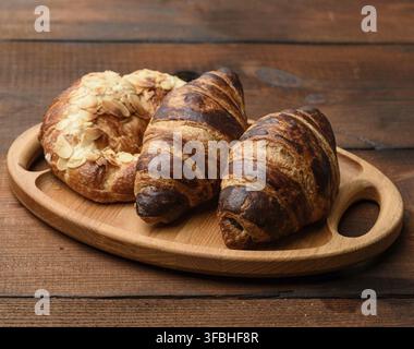 Two baked croissants lie on a wooden tray, food on a brown background Stock Photo