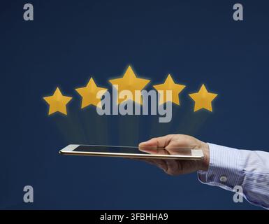 A female hand holds an electronic tablet and five yellow virtual stars above the screen. User rating of the application, service. Quality Rating Stock Photo