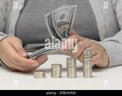 Stack of coins on white chtoli and female hands are holding a stack of paper American dollars. The concept of budget control, accumulation, profit mak Stock Photo