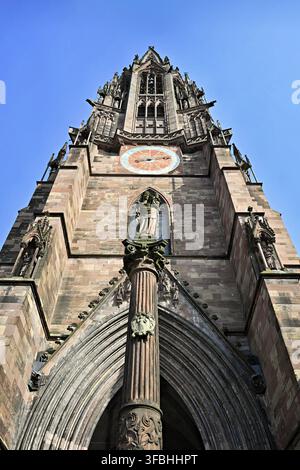 The towering tower of Freiburg Minster made of red sandstone, taken from a frog's eye view against a clear blue sky, detailed Gothic architecture with Stock Photo